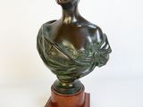 buste en bronze d'une femme posé sur un socle en bois, sur fond blanc