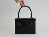 la main d'une femme tenant un sac à main noir sur fond blanc