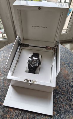 une montre dans un coffret, posée sur une table près d'une fenêtre