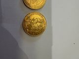 deux pièces d'or posées sur une table blanche, à côté de l'ombre d'une personne