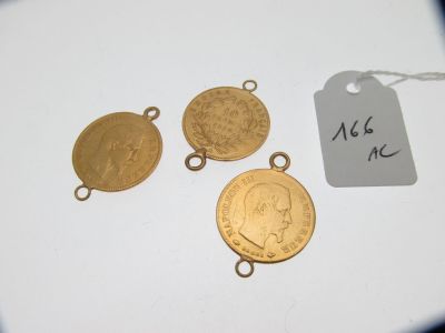 trois pièces d'or sont posées sur une surface blanche, accompagnées d'une étiquette de prix