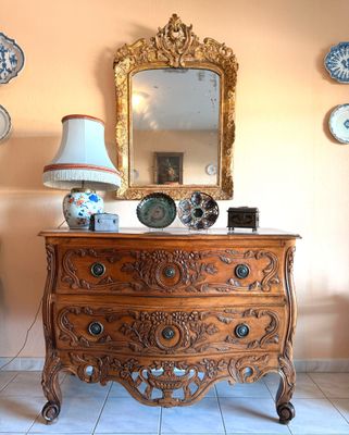 une commode surmontée d'un miroir, dans une pièce où des assiettes sont accrochées au mur
