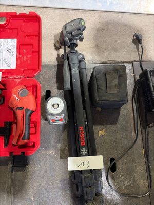 une boîte à outils rouge contenant un marteau, une perceuse, un marteau et d'autres outils, posée par terre