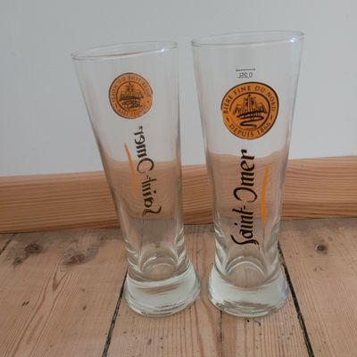 two beer glasses sitting on a wooden floor next to each other