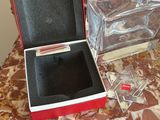 a red box with a black lid sitting on a table next to a glass vase