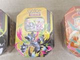 three tins of pokemon toys are lined up on a table
