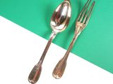 two silver spoons and a fork on a green and white surface