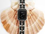 a black and silver watch on a chain with a seashell in the background