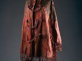 a red and black shawl with fringes on a mannequin stand