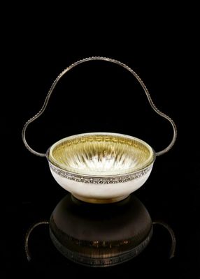 a gold and white bowl with a handle on a black surface