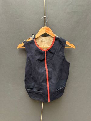 gilet bleu marine avec des bordures orange, suspendu à un cintre sur un mur gris