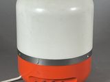 an orange and white lamp sitting on top of a table next to a gray wall