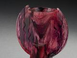 un vase en verre violet posé sur une table, devant un fond noir