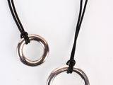 deux bagues en argent sur un collier à cordon noir, sur fond blanc