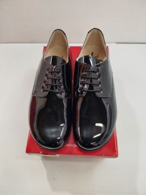 une paire de chaussures noires posée sur une boîte rouge, elle-même posée sur une surface blanche