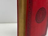 an old book with a red cover sitting on top of a white table