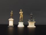 trois statues en bronze représentant un homme et une femme, posées sur des socles en marbre