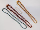quatre colliers de perles de différentes couleurs et tailles posés sur un fond blanc