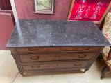 une commode avec un plateau en marbre et une chaise placée devant