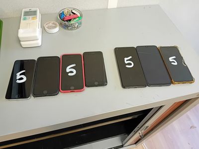 Plusieurs téléphones portables sont alignés sur une table ; des numéros y sont inscrits.