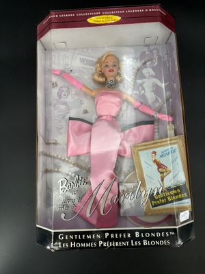 une poupée Barbie en robe rose, dans une boîte posée sur une surface noire
