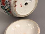 a vase with a lid sitting on a table next to a bowl