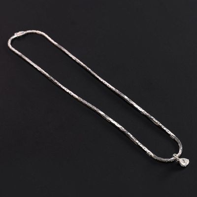 a silver necklace with a white diamond on a black background