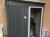 une petite remise avec un barbecue à l'intérieur, près d'une clôture