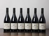 six bouteilles de vin sont posées sur une table devant un mur blanc