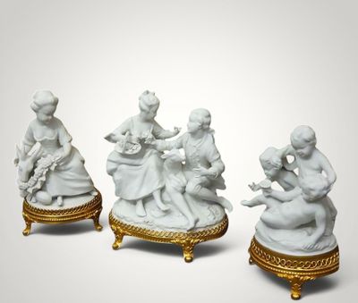 three porcelain figurines of people sitting on a gold stand