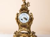 a gold clock on a white table with a beige background