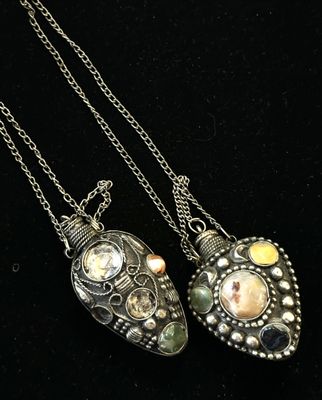 deux colliers en argent ornés de pierres de différentes couleurs, posés sur un fond noir