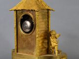a gold clock sitting on a stand with a bird on top
