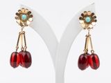 a pair of red and gold earrings on a white stand