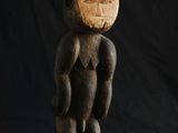 une vieille sculpture en bois représentant un homme debout, les mains sur les hanches