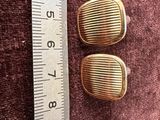pair of gold tone clip earrings on a ruler next to a ruler
