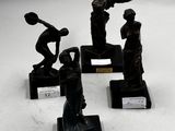 quatre figurines en bronze représentant des femmes tenant des raquettes de tennis, posées sur des socles noirs
