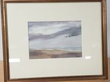 painting of a beach scene in a gold frame on a wooden table