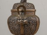 a small bronze urn on a table with a statue on top of it