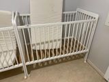 a baby crib with a mattress and a crib bed in the corner