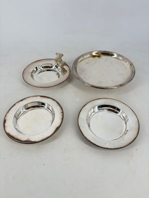trois plats en métal argenté et une assiette en argent sur un fond blanc