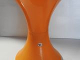 un tabouret orange posé sur une table blanche, à côté d'un mur blanc