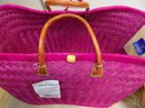 pink basket with brown handles on a wooden floor next to a cardboard box