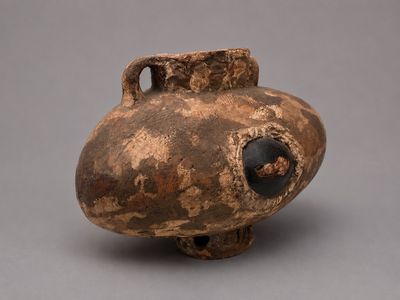 un vase marron muni d'une anse noire sur un fond gris