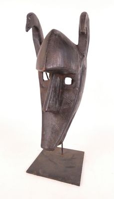 une image représentant une sculpture représentant un masque posé sur un socle en bois