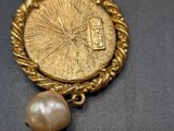 an image of a gold coin with a pearl hanging from it ' s side