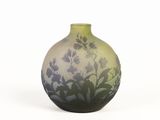 a green vase with purple flowers on it on a white surface