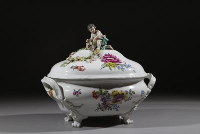 un bol blanc muni d'un couvercle, sur lequel est posée une figurine