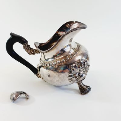 a silver teapot with a black handle and a silver spoon