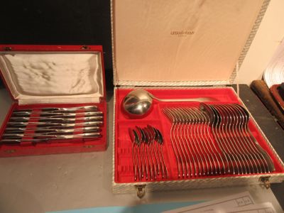 des couverts rangés dans un coffret rouge, posés sur une table à côté d'autres couverts